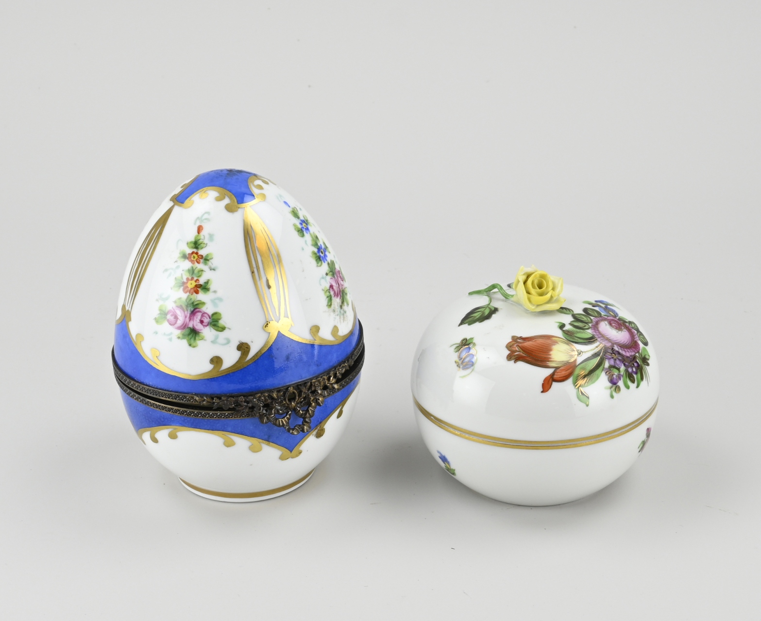 Two hand-painted porcelain lidded boxes. 20th century. 1x Limoges, egg-shaped with floral/gold decor. 1x Herend, floral/gold decor, chip rose.